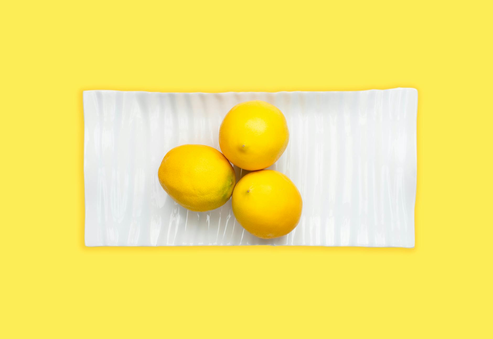 Fresh lemons arranged on white plate with yellow background, symbolizing the gentle, modern design philosophy of Hello Nancy products