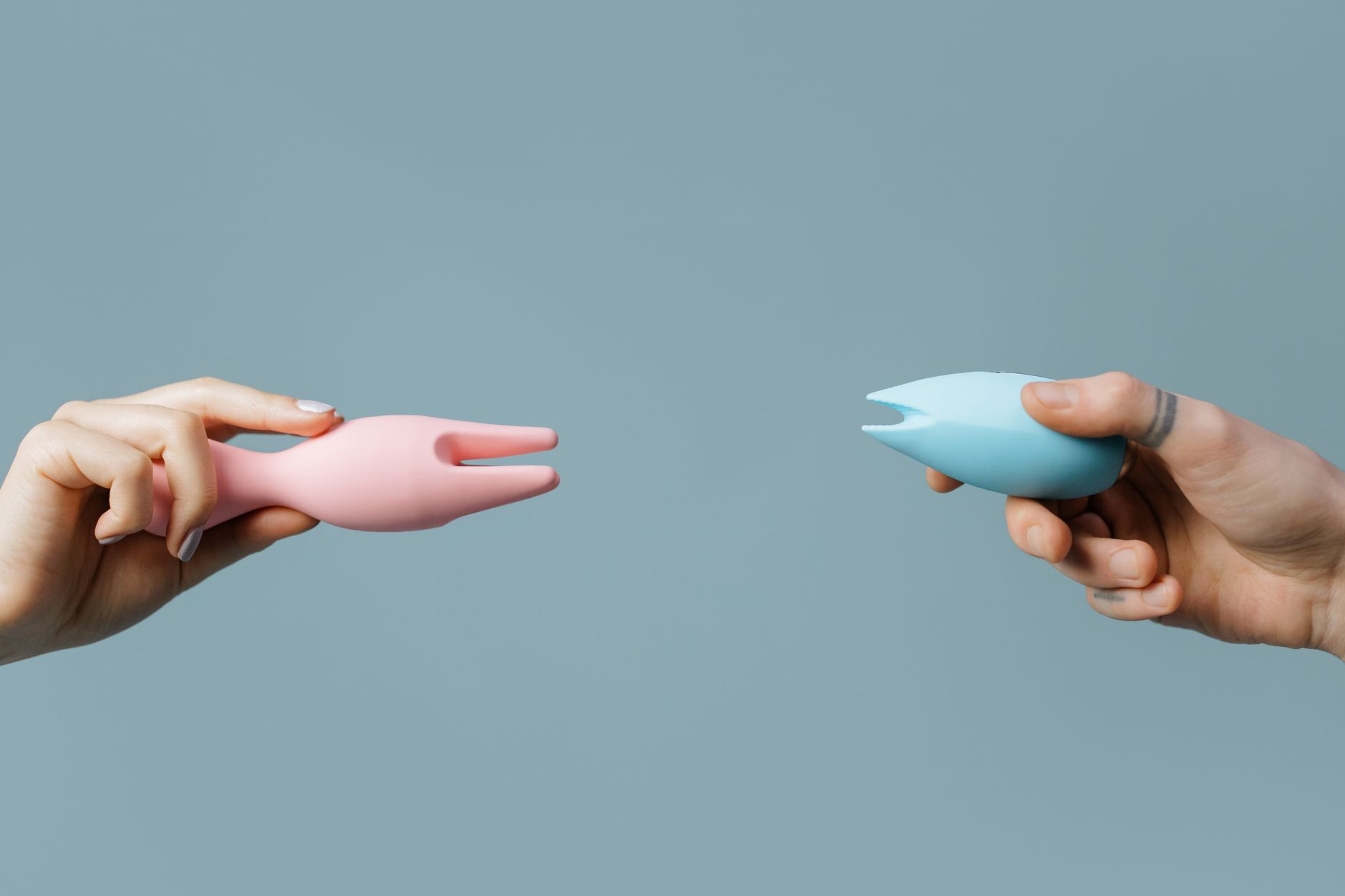 Two hands holding vibrators against a pastel background