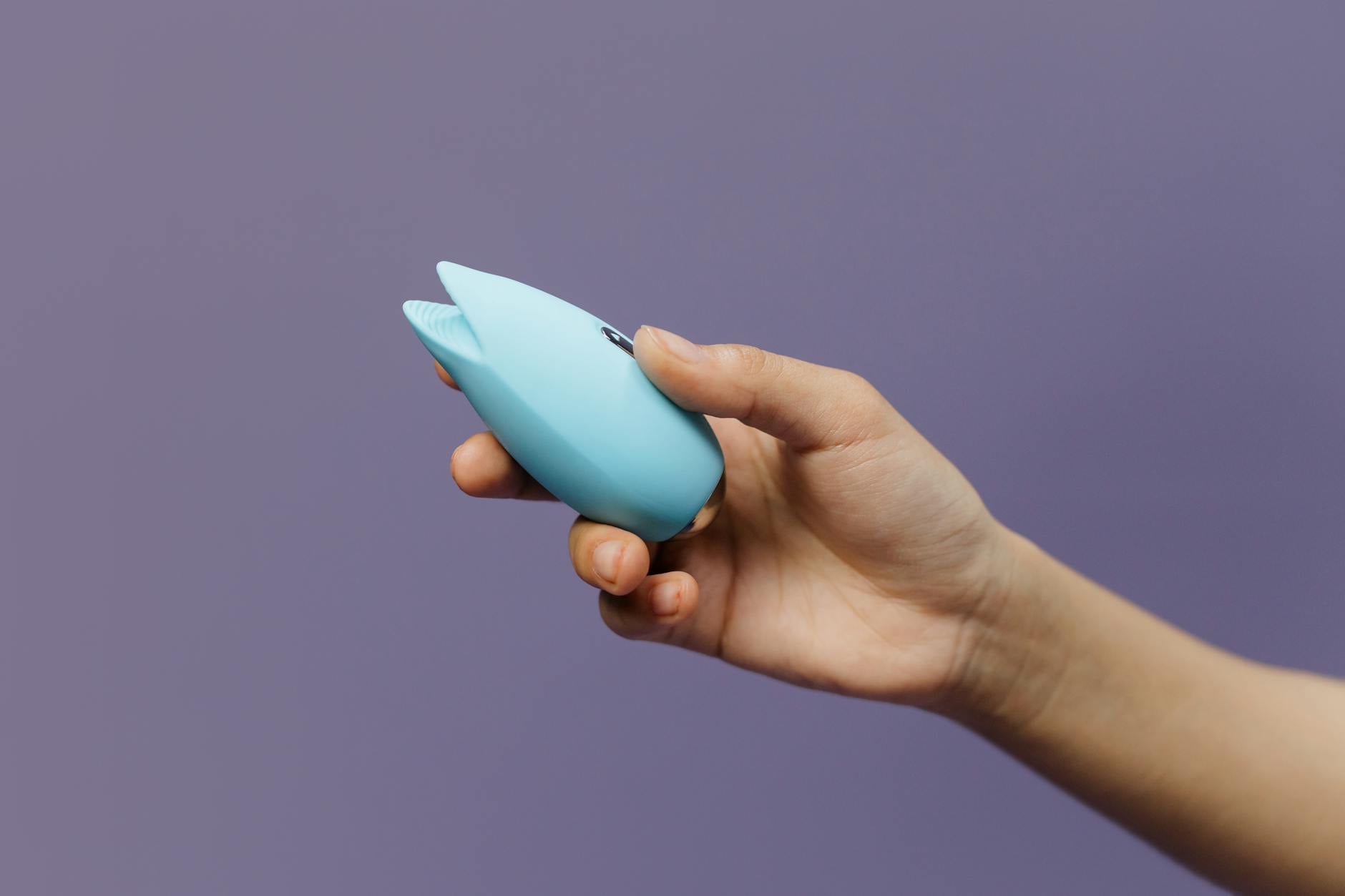 Hand holding a blue lemon clitoral vibrator against a purple background