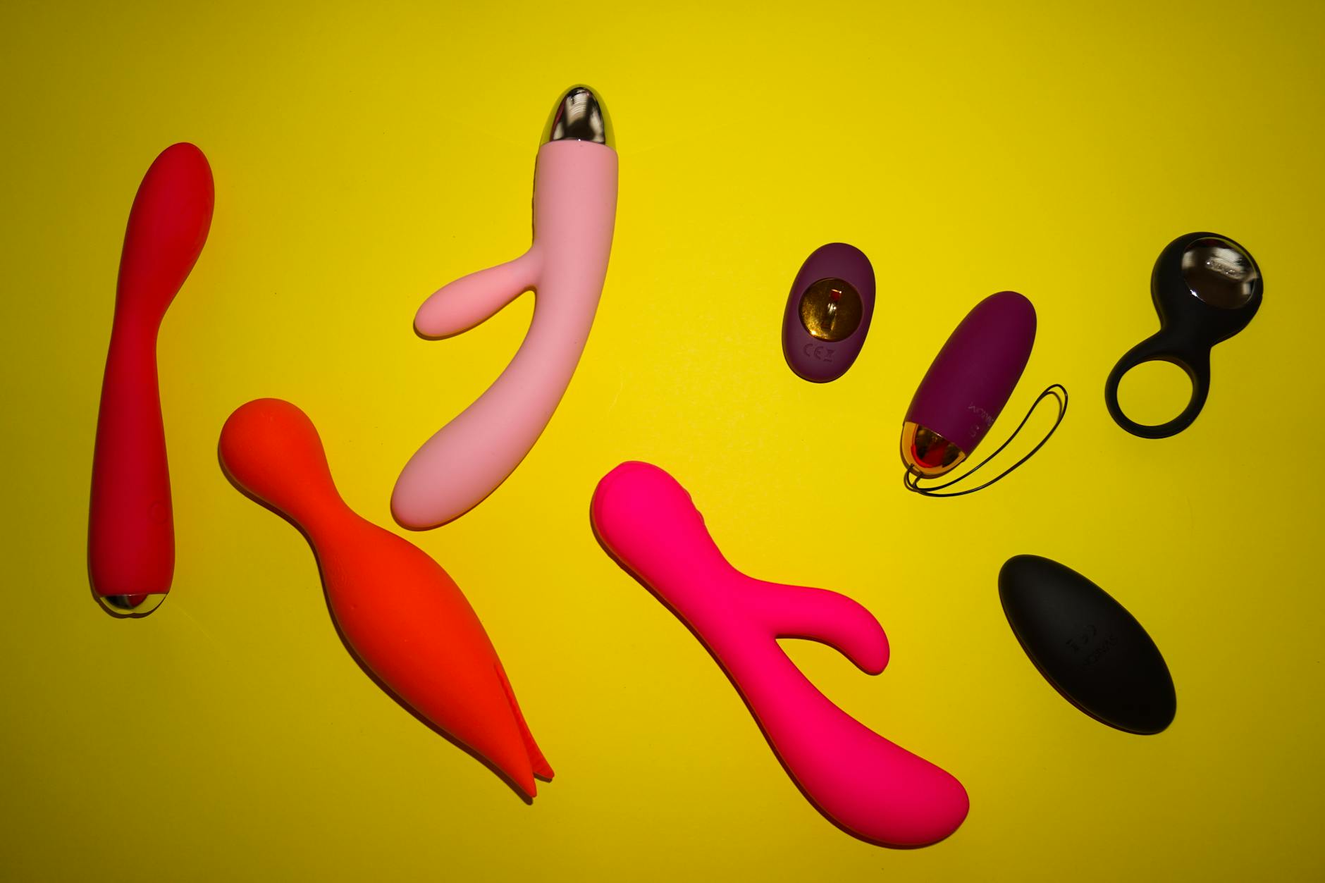 Vibrant arrangement of various clitoral vibrators and personal massagers on a bright yellow surface