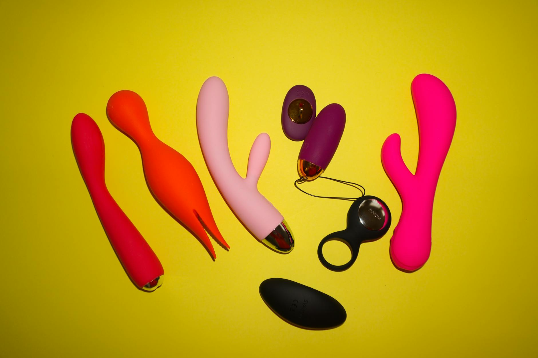Colorful vibrators arranged on a bright yellow background, featuring various clitoral vibrators and designs